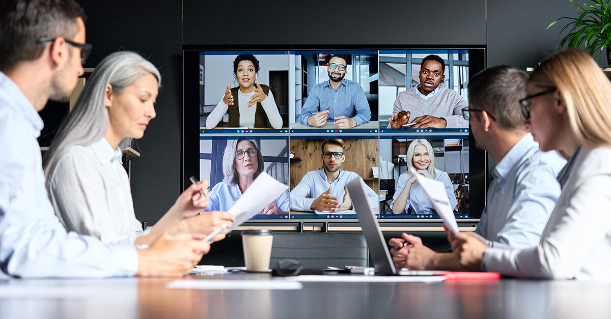 Global corporation online videoconference in meeting room with diverse people sitting in modern office and multicultural multiethnic colleagues on big screen monitor.
